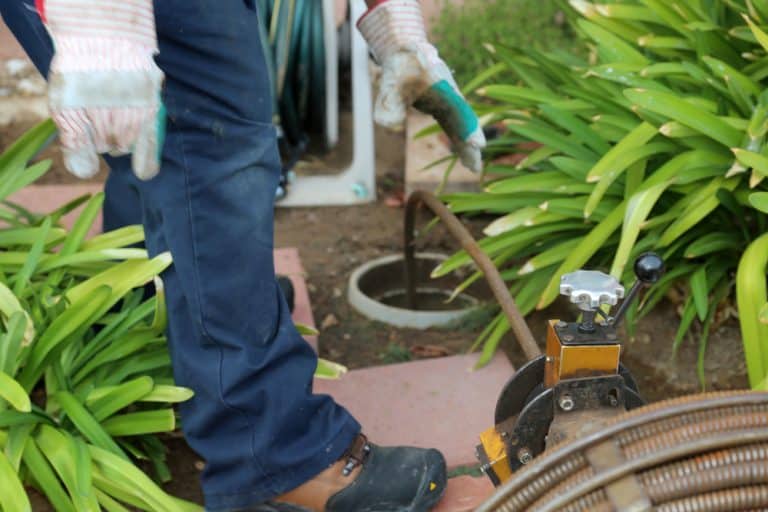 sewerage workers draining sewer line using snake to clean